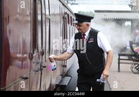 Wansford, UK. 15th Aug, 2020. A Porter cleans the handles on the carriages as the Nene Valley Railway have resumed running steam trains from Wansford to Peterborough after the COVID-19 Coronavirus pandemic forced them to stop during lockdown. The 92 Squadron Battle of Britain 34081 steam train has been prepared and is ready to go, with the carriages having their capacity reduced to allow for new social distancing guidelines. Credit: Paul Marriott/Alamy Live News Stock Photo