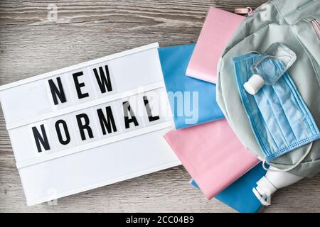 Lightbox with text NEW NORMAL protective face mask and sanitizer. Back to school. Books falling from backpack. Social distancing Stock Photo