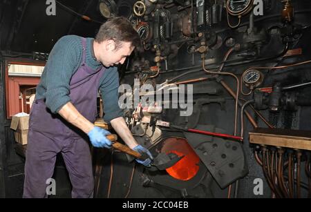 Wansford, UK. 15th Aug, 2020. Jack Colby feeds the fire with coal as The Nene Valley Railway have resumed running steam trains from Wansford to Peterborough after the COVID-19 Coronavirus pandemic forced them to stop during lockdown. The 92 Squadron Battle of Britain 34081 steam train has been prepared and is ready to go, with the carriages having their capacity reduced to allow for new social distancing guidelines. Credit: Paul Marriott/Alamy Live News Stock Photo