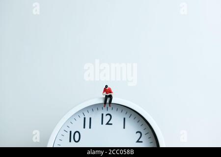 Miniature people for morning reading time concept - young man seating above clock reading a book Stock Photo
