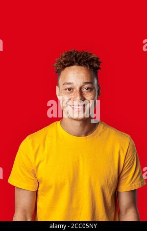 Freestyle. Mulatto freckled guy in yellow t-shirt standing isolated on dark pink smiling cheerful Stock Photo