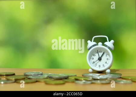 time is money concept - pile of money with white clock on a wooden table Stock Photo