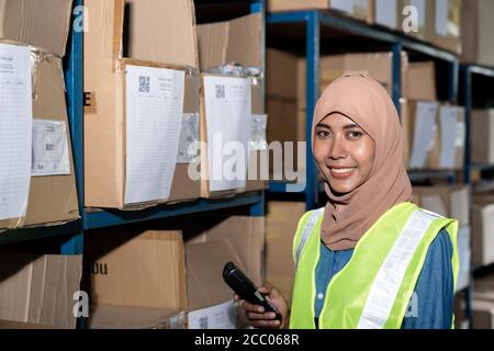 Portrait of Islam Muslim female warehouse worker hold barcode scanner in front of product shelf with stock card in warehouse distribution. For busines Stock Photo