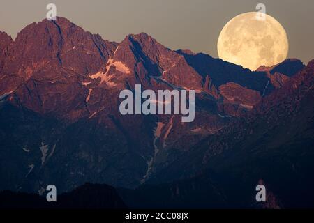 full moon setting behind the top of the mountain lit by the sun just rising Stock Photo