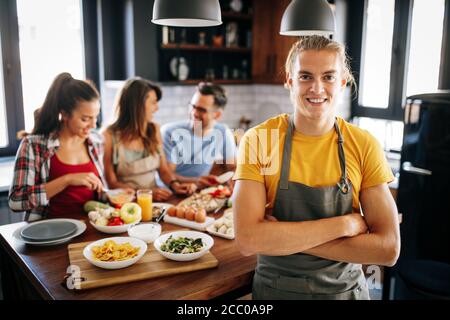 Group of happy friends laughing and talking while preparing meals in kitchen Stock Photo