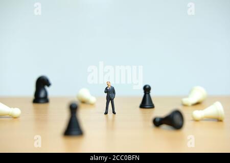 Miniature people strategic concept - businessman standing between losses / dropped pawn Stock Photo