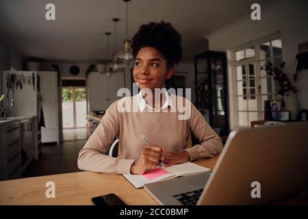 Successful young entrepreneur thinking while writing in diary and using laptop at home using coronavirus lockdown Stock Photo