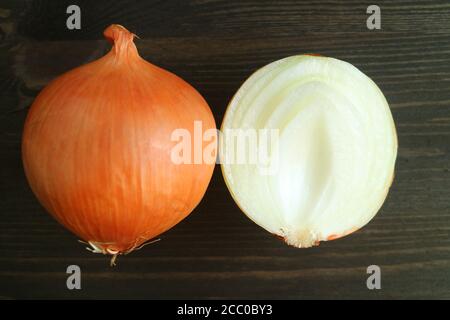 The unpeeled with cut in half onions isolated on dark color wooden background Stock Photo