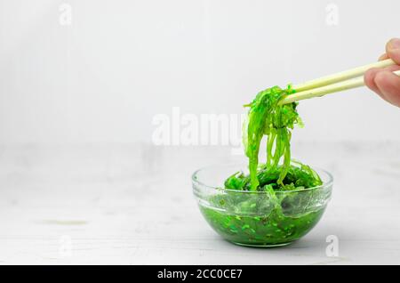 Green wakame seaweed salad in some transparent glass bowls, on a white wooden table Stock Photo