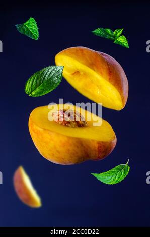 Sliced fresh peach with mint leaves, isolated on a black background. Fruit levitation, flying food Stock Photo