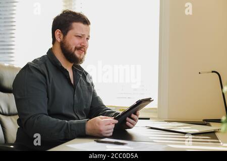 Male employee using tablet at office, laptop on desk. Stock Photo