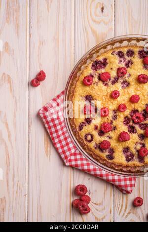 Sweet tasty pie with jellied and fresh raspberry fruits in baking dish with red tablecloth towel, wooden table background, top view Stock Photo