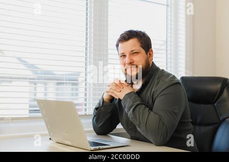 Smiling computer hacker sitting working online with laptop at cabinet. Stock Photo