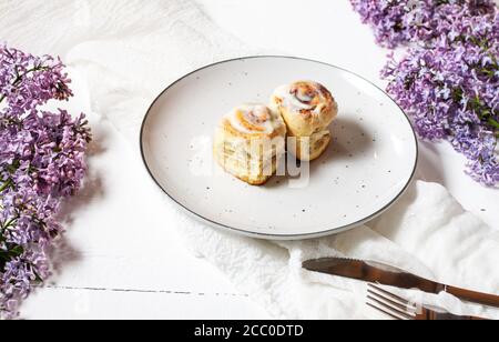 Cinnamon roll or cinnabon with white cream glaze on plate on white wooden background. Traditional homemade sweet buns Stock Photo