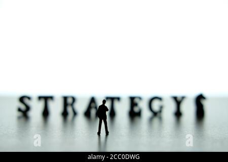 Silhouette of miniature businessmen standing and thinking in front of strategy word block puzzle