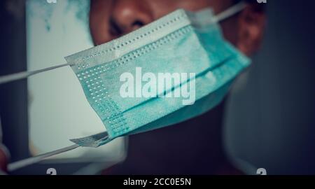 Black woman putting on or taking off her face mask. Selective focus on the mask. Blurry background, Stock Photo