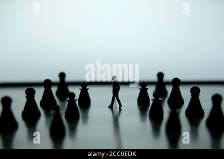 Business strategy conceptual photo - Miniature of businessman walking forward in the middle of chess piece on a chessboard Stock Photo