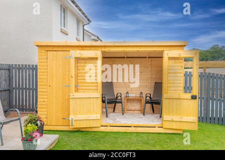 A newly erected summer house , garden room in natural stained cabin finished wood surrounded by newlly laid turf and painted silver copse paint. A goo Stock Photo