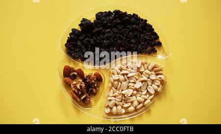 Top closeup view of delicious nuts in plastic transparent containers on yellow background Stock Photo