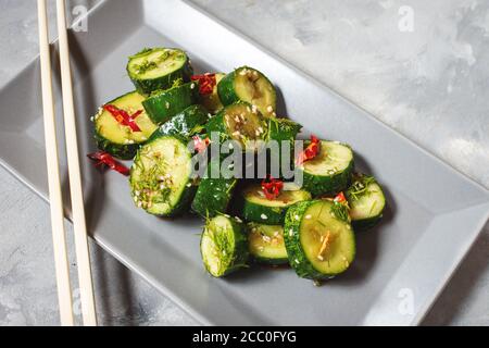 Asian beaten cucumber salad with chili and sesame seeds on a concrete background. Chinese food concept. Stock Photo