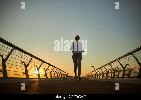 Cheerful woman running on the bridge during sunrise