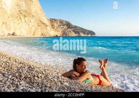 Portrait of a girl in swimsuit lying on pebbles beside the water at Porto Katsiki beach, Lefkada, Ionian Islands, Greece