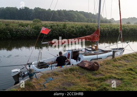 With rods over the deck of his small yacht, a man fishes for perch on the still waters of the river Chet, on 13th August 2020, in Loddon, Norfolk, England. Stock Photo