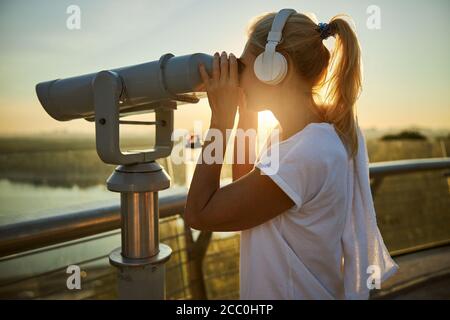 Charming woman in wireless headphones using street binoculars Stock Photo