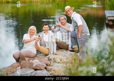 Group of happy seniors sitting by the lake in summer with a glass of water Stock Photo