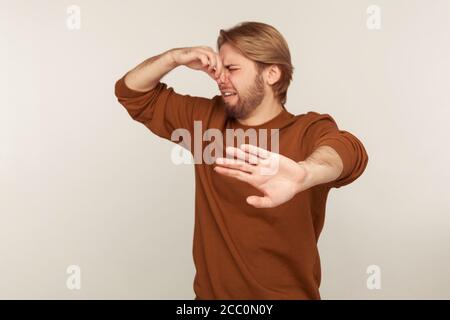 Bad smell. Portrait of confused bearded man grabbing nose, grimacing in disgust and showing stop gesture, expressing repulsion to stink, fart gases, i Stock Photo