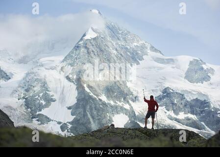 Back view of male hiker pointing at amazing view, rocky mount Ober Gabelhorn in snow in the Pennine Alps in Switzerland, located between Zermatt and Zinal Stock Photo