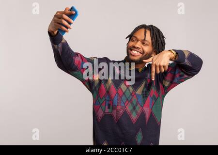 Please like and subscribe. happy african blogger man with dreadlocks in sweatshirt making video live on social media and having fun with his followers Stock Photo