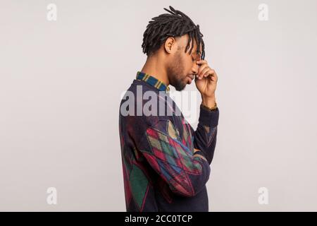 Profile portrait of deeply upset frustrated bearded african man with dreadlocks touching his face with hand, facepalm, depression. Indoor studio shot Stock Photo