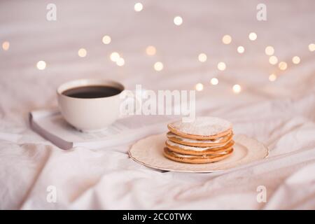 Stack of creamy pancakes with open book and fresh coffee over glowing lights closeup. Good morning. Breakfast time. Stock Photo