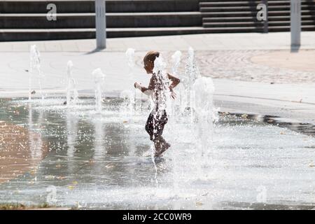 A child plays in the water fountains in Priory Street, Coventry. The fountains situated between the university, Cathedral and Herbert art gallery rise and fall and are a feature of the city centre. Coventry is to become city of culture in 2021. Stock Photo