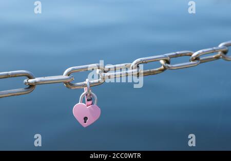 Love padlocks in pink hanging on metal chain fence Stock Photo