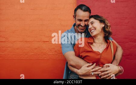 Beautiful couple in love embracing standing against a wall. Romantic couple together on multicolored wall. Stock Photo