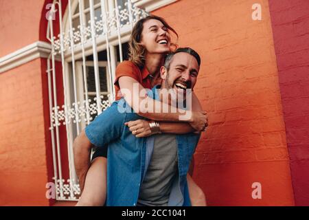 Mature man carrying his girlfriend on his back walking on the city street. Couple piggybacking on city street. Stock Photo