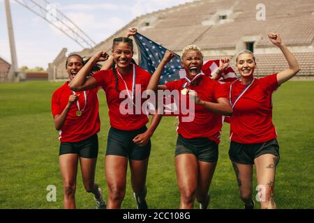 Female soccer players running on field shouting in joy after winning the championship. American female football team celebrating championship, screami Stock Photo