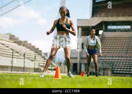 Female footballers practicing ball control by dribbling around orange cones on the field. Female footballers improving agility with running drills. Stock Photo