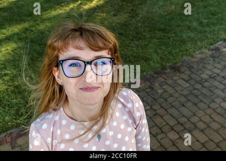 Happy redhead girl with glasses looking at the the camera from the bottom up Stock Photo