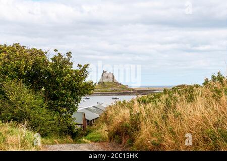 Looking across from a Heugh path descending to the small harbour at Holy Island with a few small pleasure or fishing boats towards Lindisfarne Castle Stock Photo