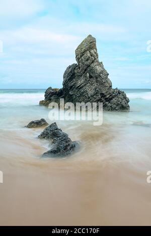 Sea stack and rocks on a golden beach as the tide comes in Stock Photo