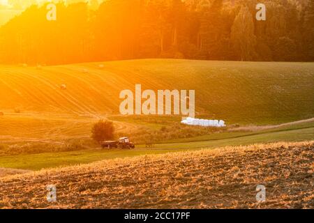 Sunset over rural fields with tractor and golden sunlight. Dusk in the countryside. Stock Photo