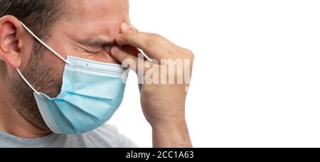 Close-up of thinking adult man touching forehead using fingers as stress headache concept wearing medical or surgical covid19 protection mask with cop Stock Photo
