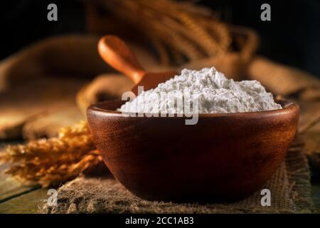 Flour in a bowl with a floured spoon, on a rustic wooden background. Close up, side view, high-resolution product image. Stock Photo