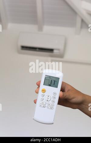 Young woman using a remote control of wall-mounted air conditioner. Stock Photo