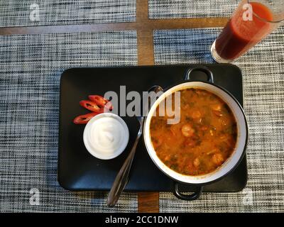 Hungarian spicy soup. Served on a black porcelain tray in a deep bowl. On a tray is a small bowl with sour cream and pieces of red pepper. Nearby is a Stock Photo