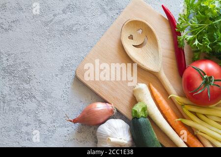 Vegetables, cutting board and smiling spoon on concrete background. Healthy eating concept Stock Photo