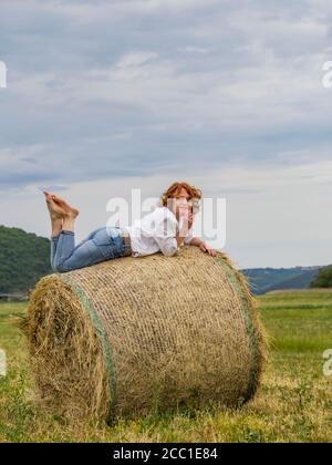 Mature woman on hay haystack in field Stock Photo